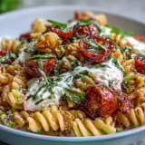 Burrata-topped Caprese pasta with burst cherry tomatoes, fragrant basil, and a drizzle of olive oil on a white plate.