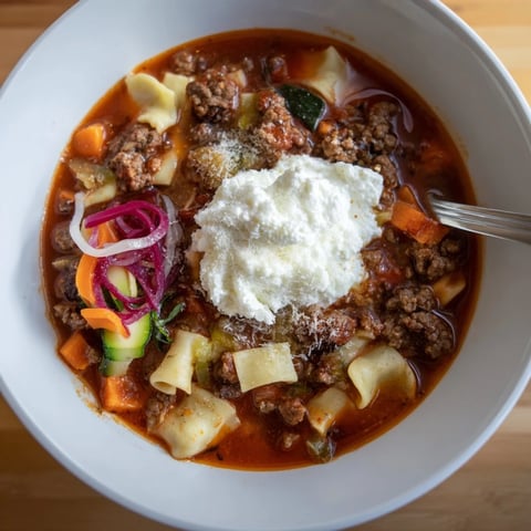 Hearty lasagne soup steaming in a bowl, topped with zesty pickled vegetables.  