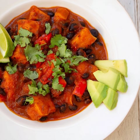 Steaming bowl of Sweet Potato & Black Bean Chili, garnished with fresh cilantro and a lime wedge.