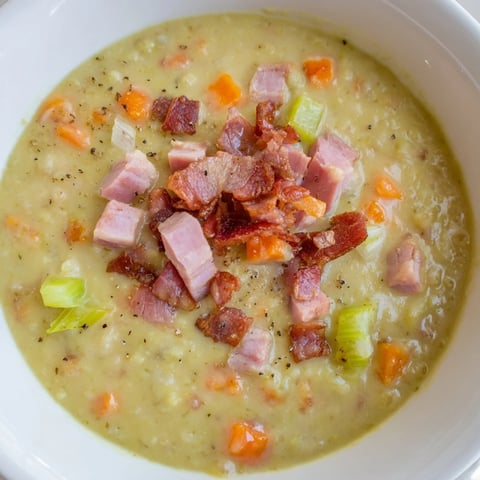 Hearty split pea soup with ham and bacon: a steaming bowl featuring crispy bacon and tender veggies.
