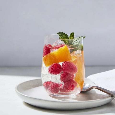 Vibrant sparkling juice with raspberries, adorned with orange slices and mint, ready to enjoy.