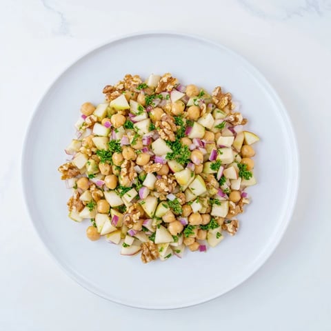Fall Harvest Apple and Chickpea Salad: A colorful mix of apple pieces, chickpeas, and walnuts glistening with dressing.
