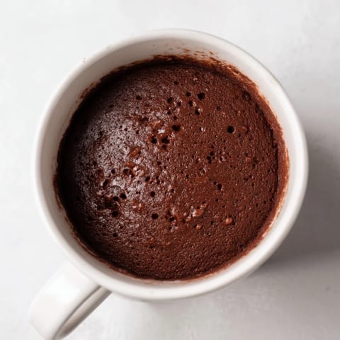 A close-up shot of a fluffy, warm microwave mug cake topped with whipped cream.