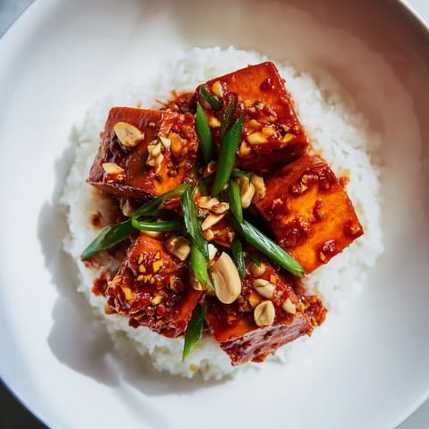 A close-up of delicious Chinese Mapo Tofu, glistening with a spicy chili sauce and garnished with scallions.