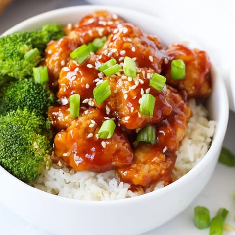 A close-up of a Sweet Chili Chicken Bowl, garnished with green onions and sesame seeds beside a fork.