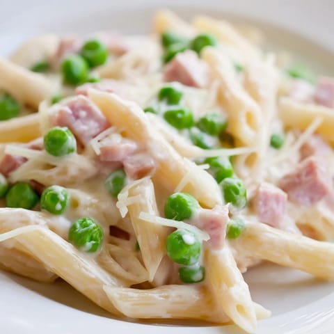A steaming skillet of Spring Pea & Ham Pasta tossed in a creamy Parmesan sauce, with a wooden spoon ready to serve for an easy dinner.