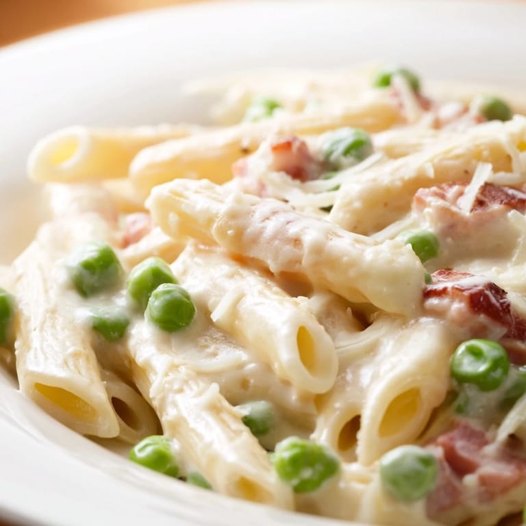 Spring Pea & Ham Pasta plated with al dente penne, sweet peas, and caramelized ham, topped with grated Parmesan and black pepper for a comforting meal.